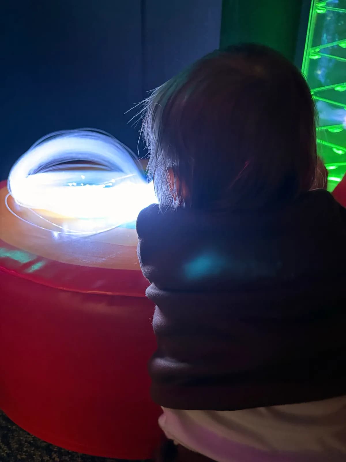 A child, seen from behind, leaning in towards softly glowing fibre-optic lights.
